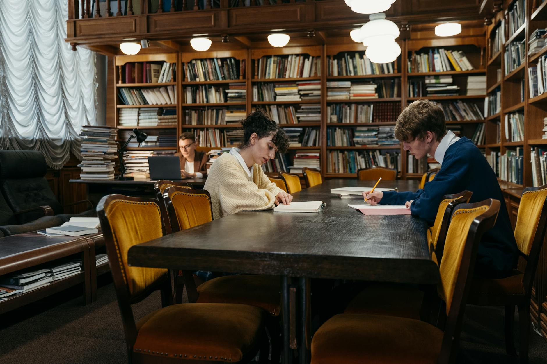 Group of students diligently studying in a traditional library filled with books, tables, and dim lighting — TransferCredit.org