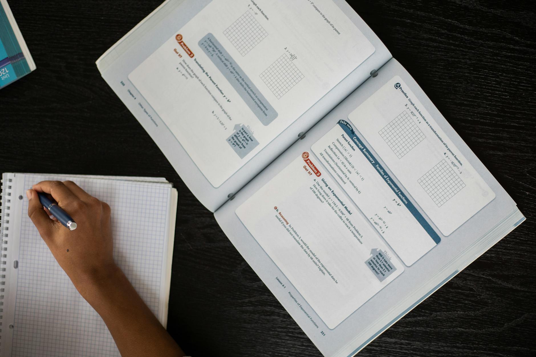 Top view of faceless African American student taking notes in notepad while sitting at table with textbook during lesson in class — TransferCredit.org
