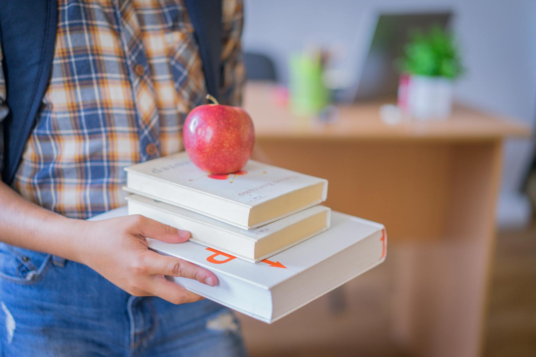 Child holding books with an apple in a classroom, symbolizing education — TransferCredit.org