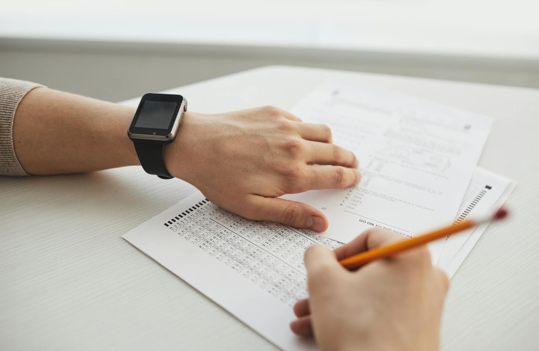Student completing a multiple-choice exam with a pencil, close-up view — TransferCredit.org