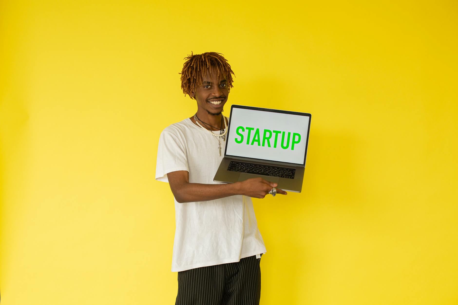 Smiling man holding a laptop with 'STARTUP' on screen against vibrant yellow background — TransferCredit.org