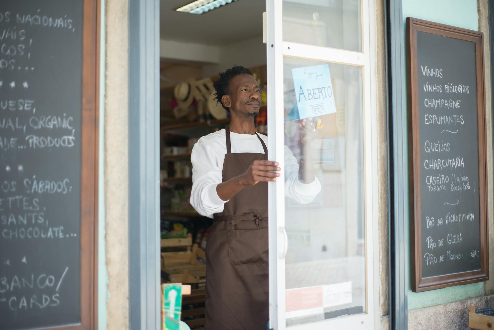 A man in an apron opens a grocery store door in Portugal, ready for business — TransferCredit.org