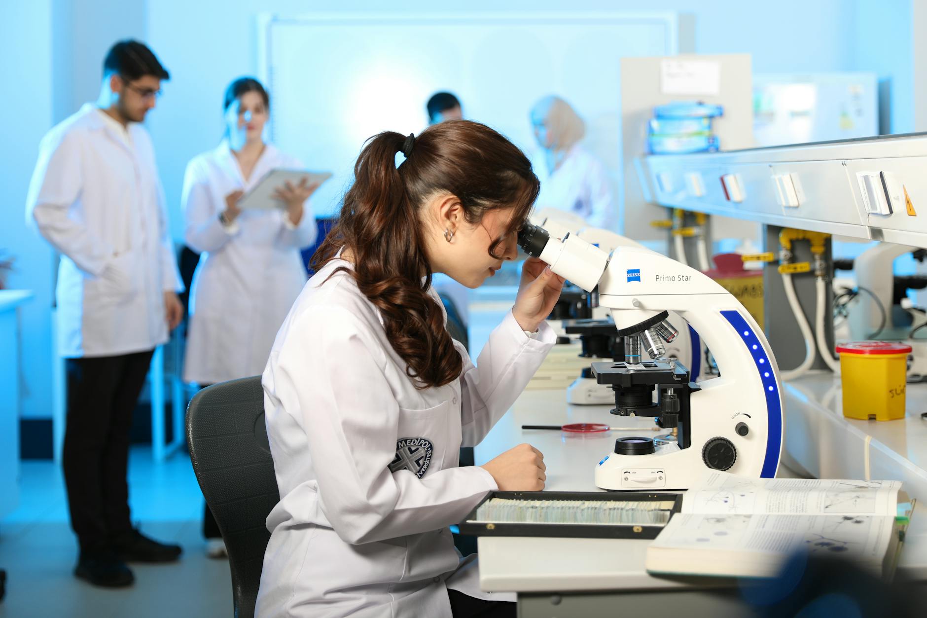 Young female scientist examining samples under a microscope in a modern laboratory setting — TransferCredit.org