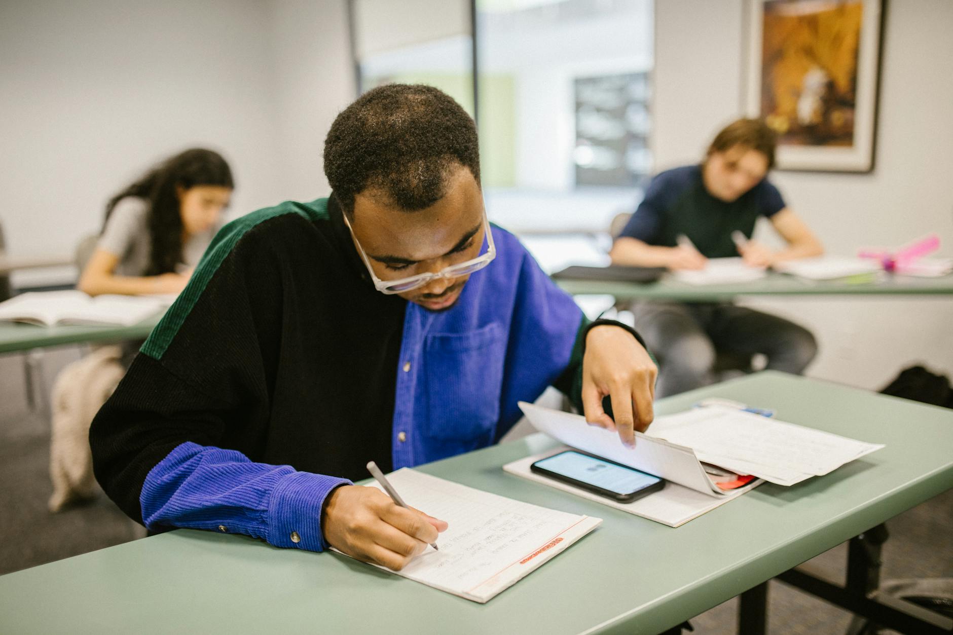 Students taking a test in a classroom setting, focusing on a man writing while others work — TransferCredit.org
