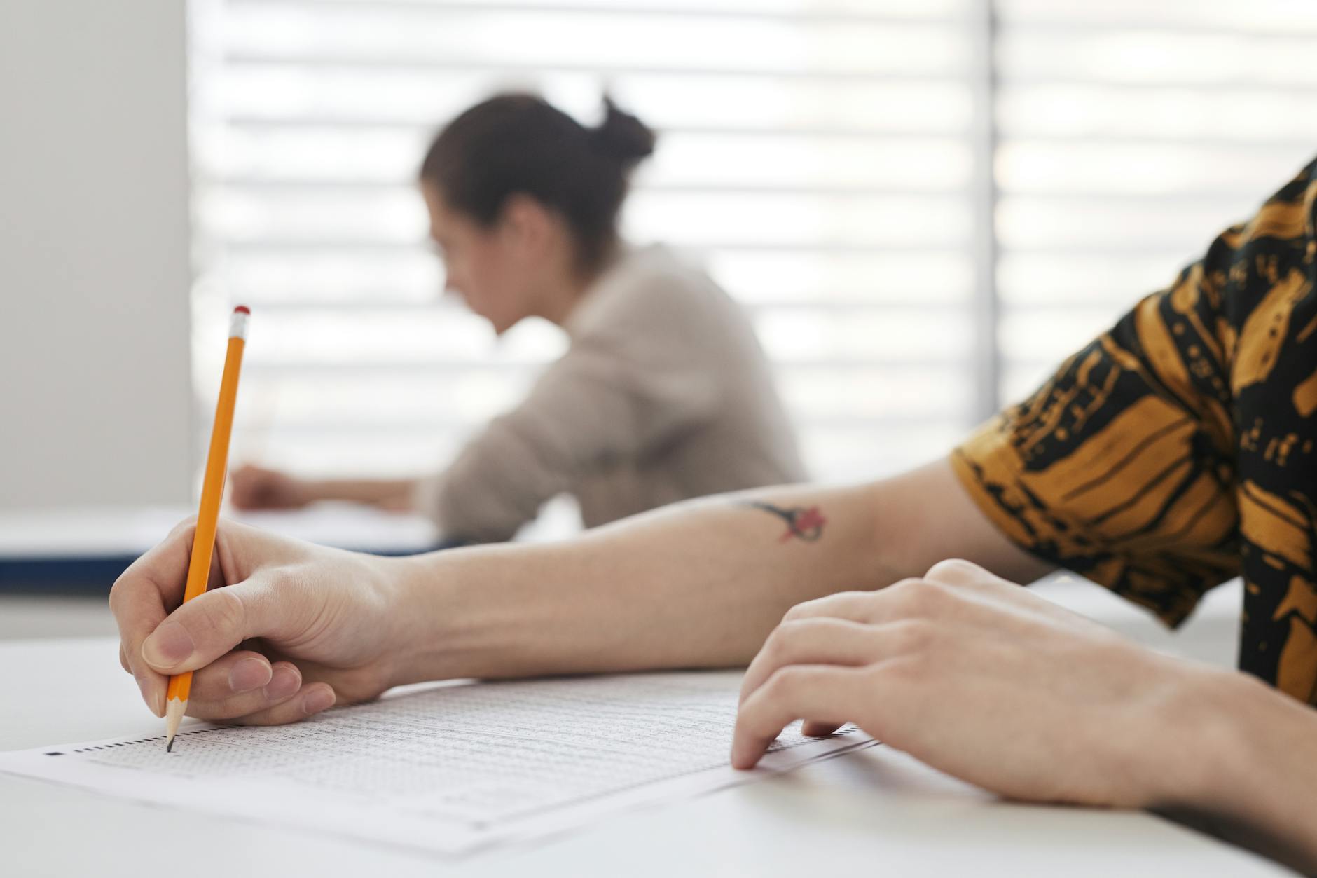 Close-up of student's hands writing on exam sheet, indoors with blurred background — TransferCredit.org