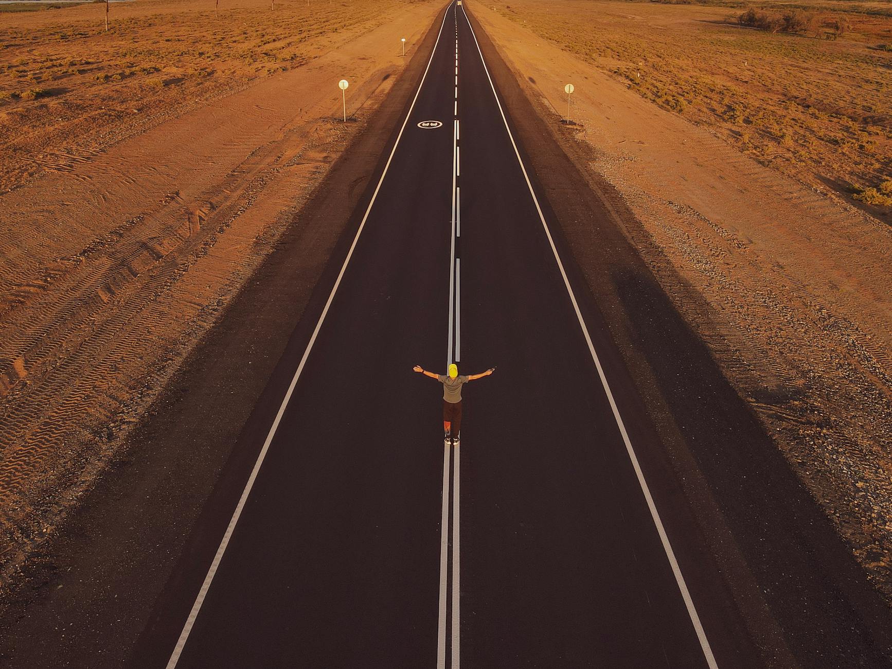 Aerial shot of a person standing alone on an empty road in a desert landscape, arms outstretched — TransferCredit.org