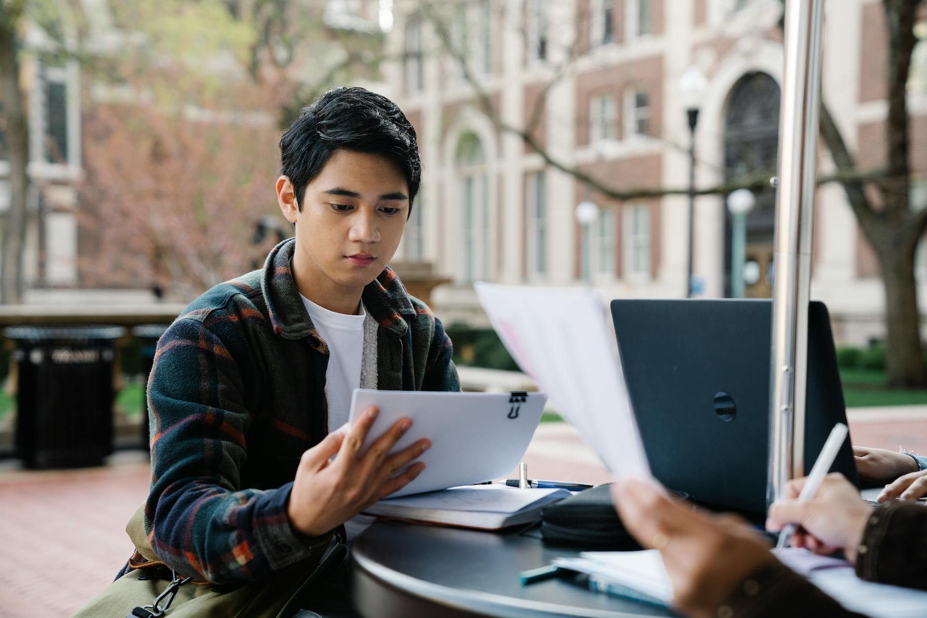 A college student reviews papers outside on campus with classmates, engaging in collaborative study — TransferCredit.org