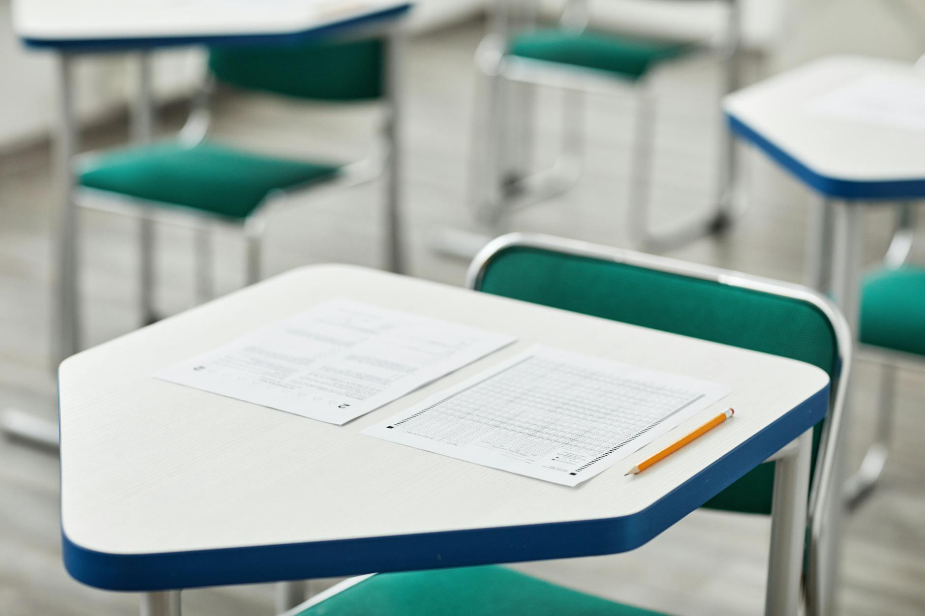 A close-up of an empty classroom desk with exam papers and a pencil, highlighting education and testing environment — TransferCredit.org