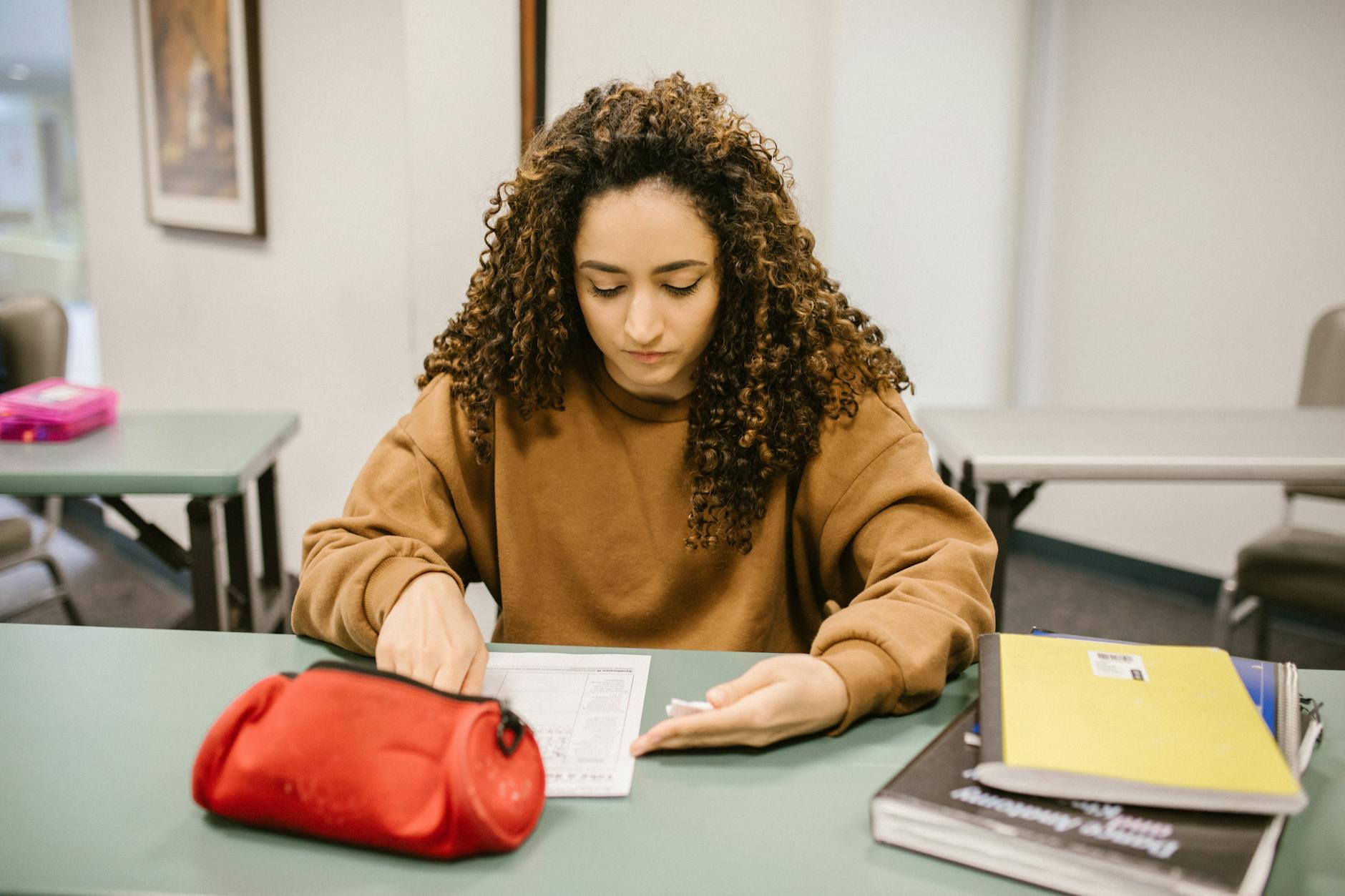 Young woman studying for an exam in a college classroom with books and notes — TransferCredit.org