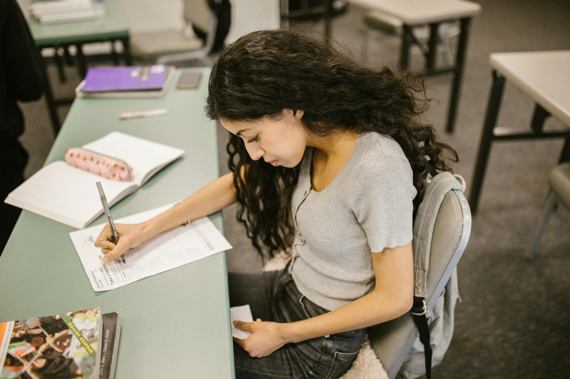 Young college student writing on test paper in a classroom setting, focused on academic success — TransferCredit.org