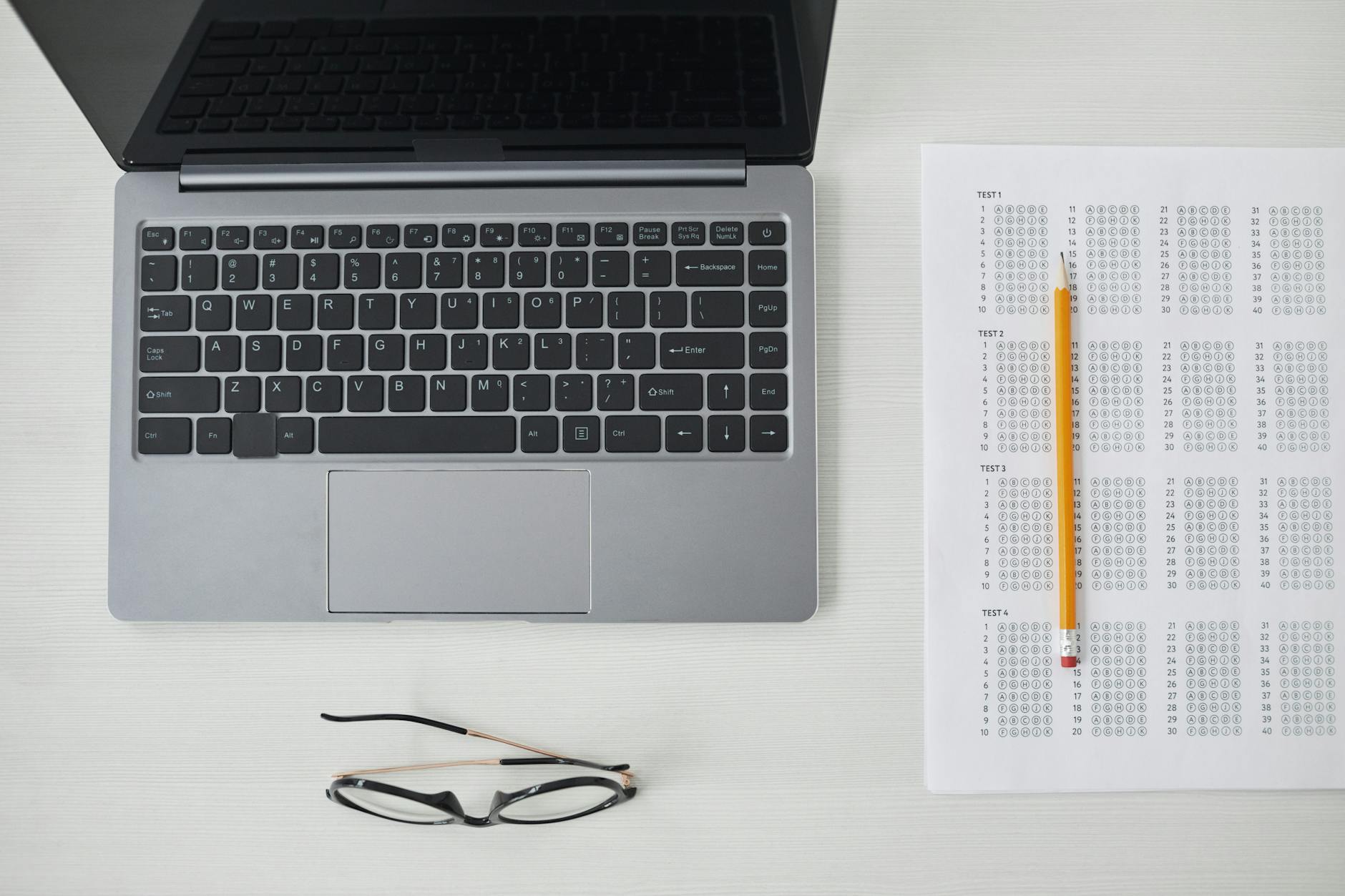 Flat lay of a laptop, exam sheet, and pencil on a white desk, perfect for education and technology themes — TransferCredit.org