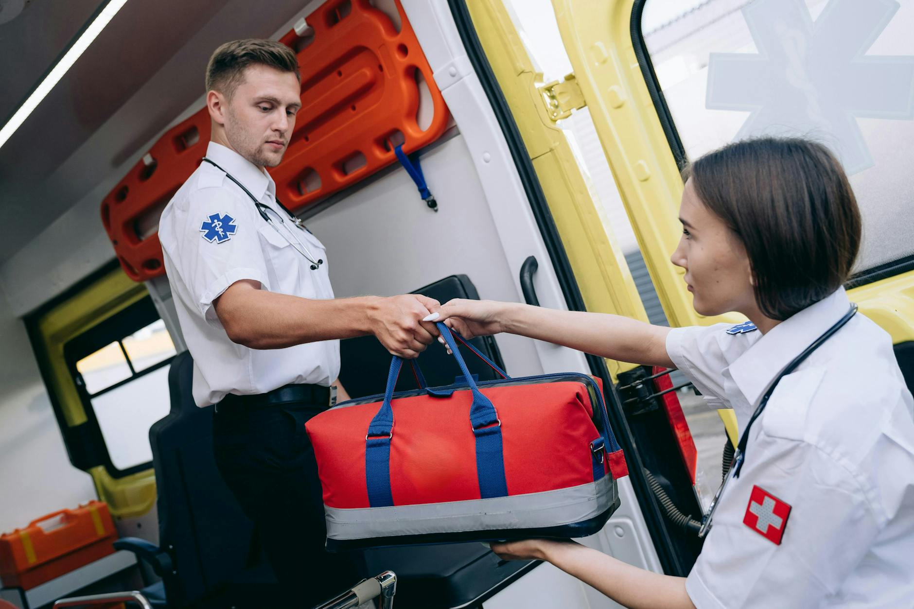 Male and female paramedics exchanging a medical kit inside an ambulance, showcasing teamwork — TransferCredit.org