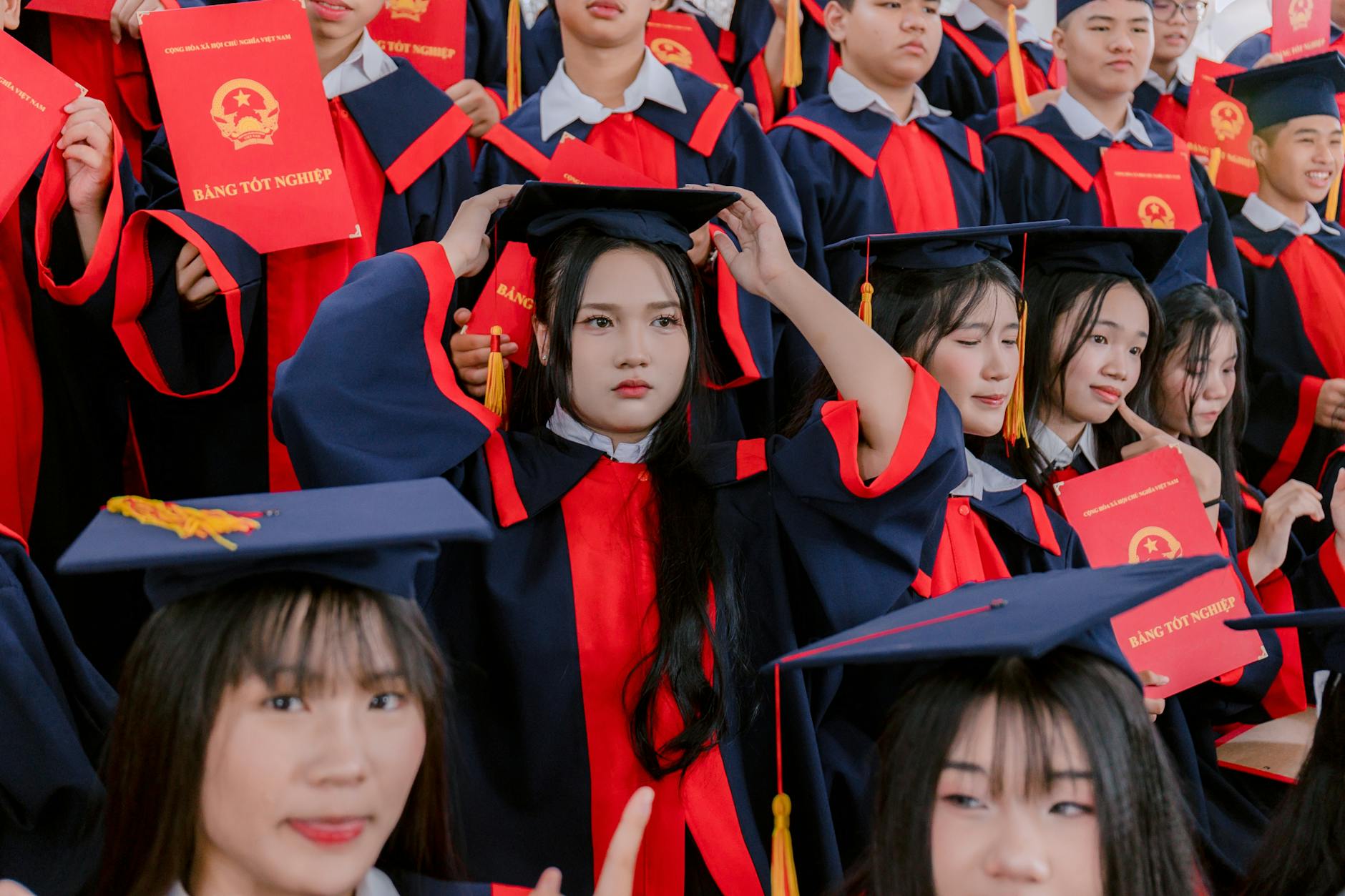 A large group of graduates in caps and gowns celebrate their ceremony, holding diplomas — TransferCredit.org
