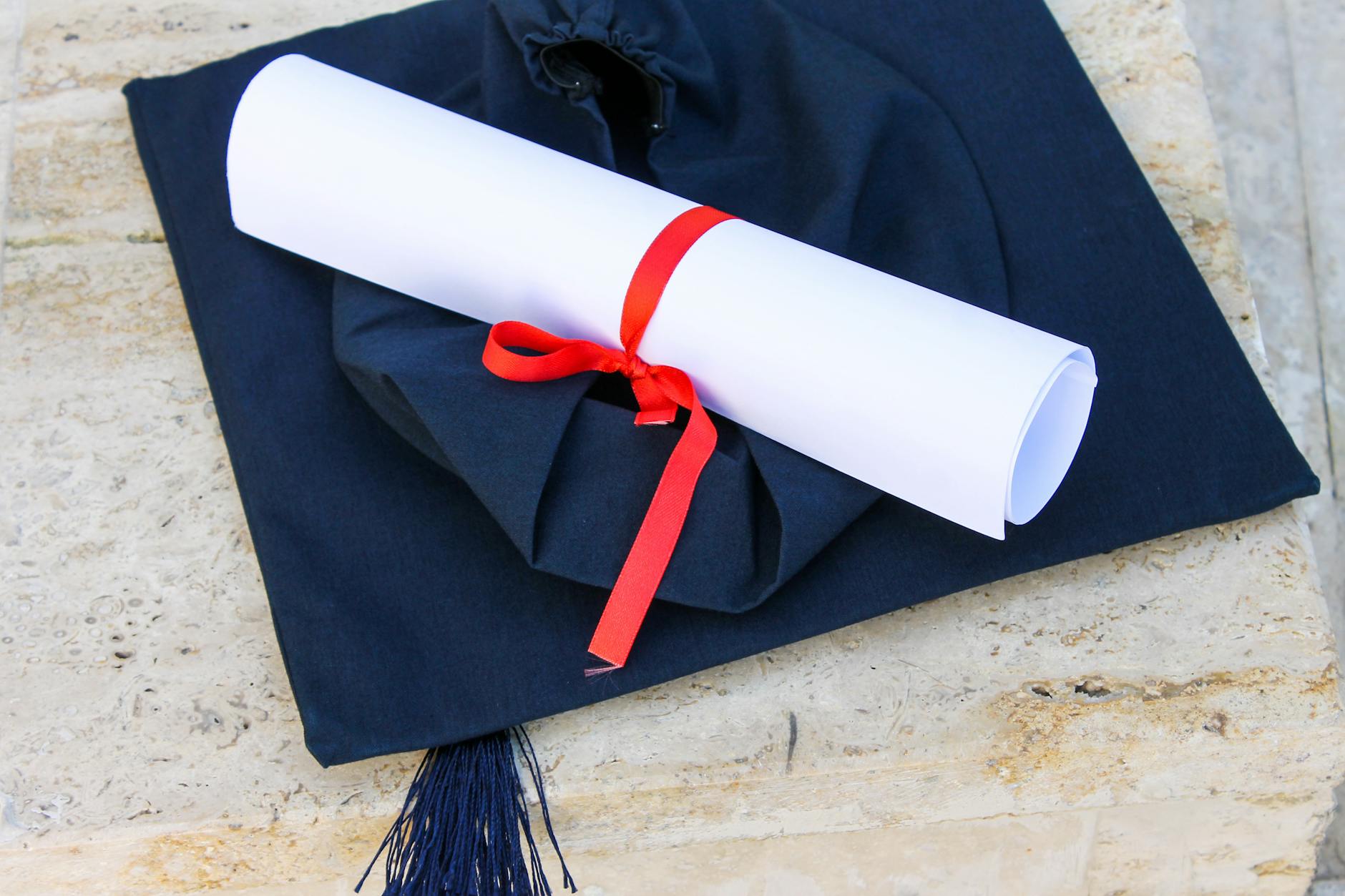 Graduation cap with diploma roll tied with red ribbon on concrete surface — TransferCredit.org