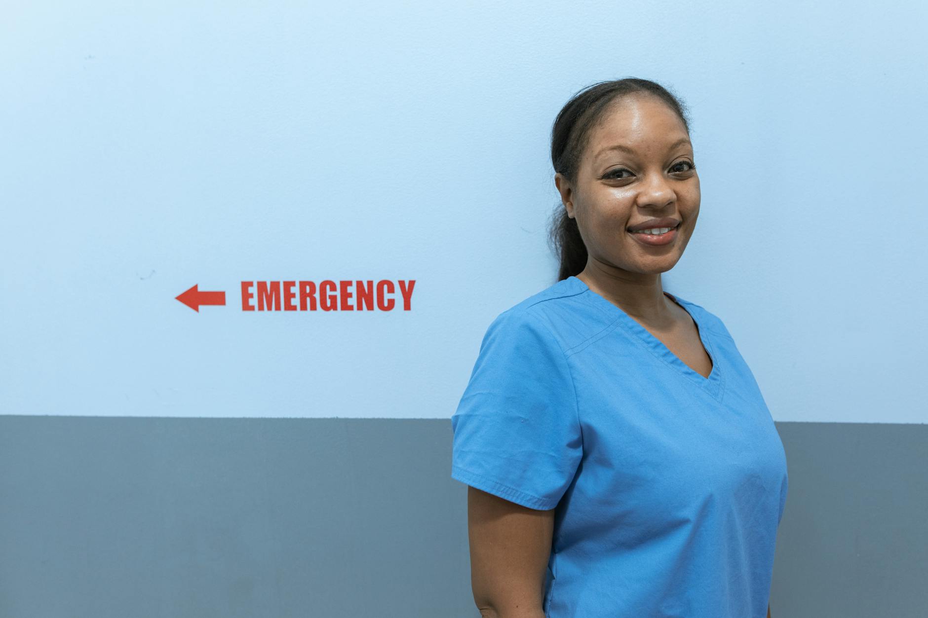 Happy healthcare worker in scrubs standing near emergency room sign — TransferCredit.org