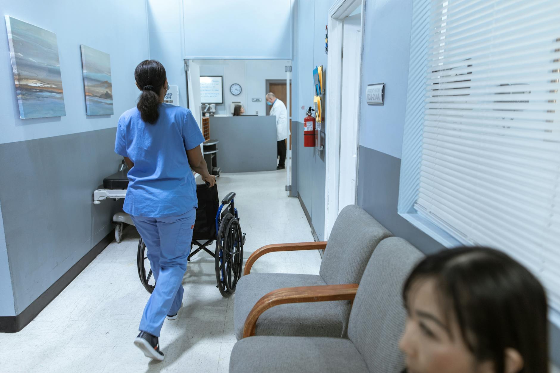 A nurse in scrubs pushes a wheelchair through a well-lit hospital corridor, attending to patient care — TransferCredit.org