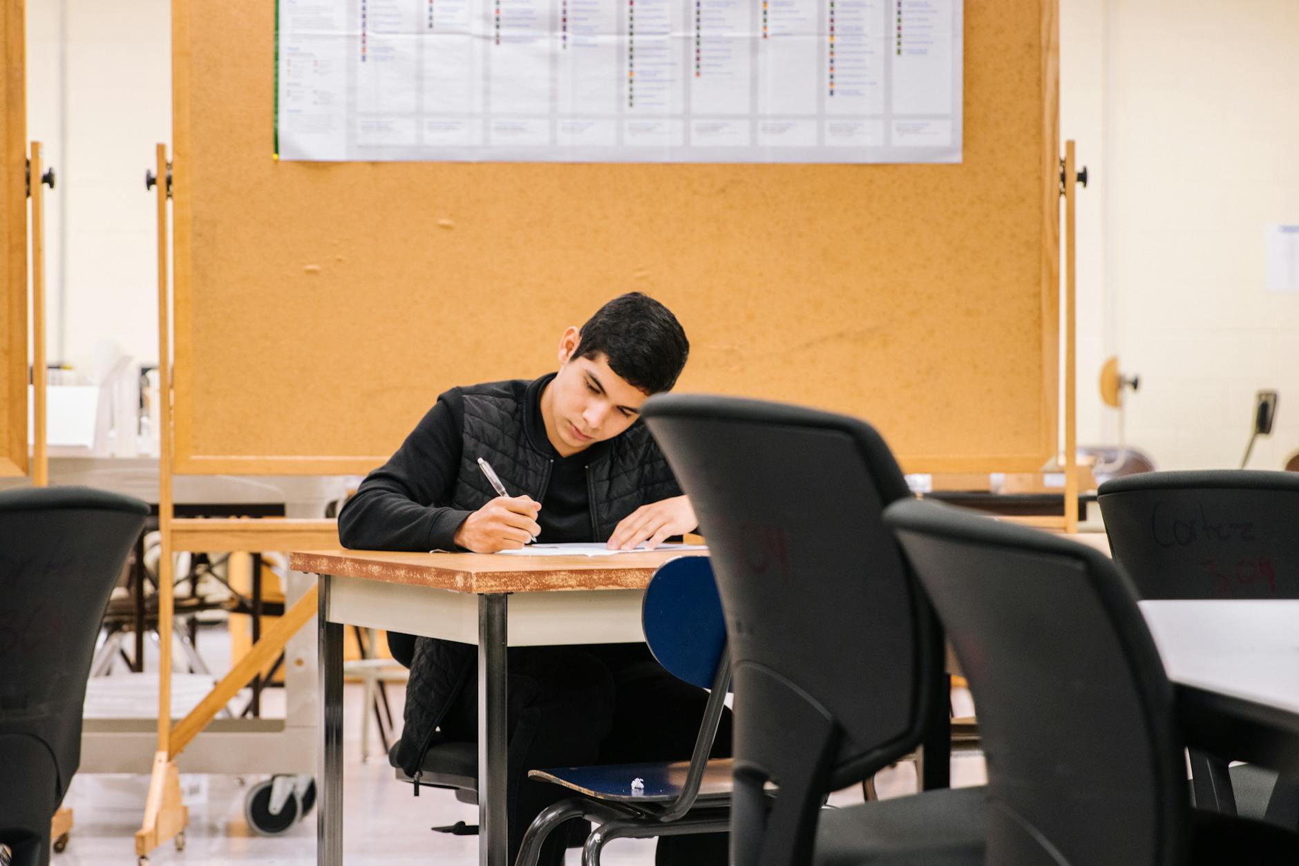 Young man focused on writing in a classroom, ideal for education concepts — TransferCredit.org