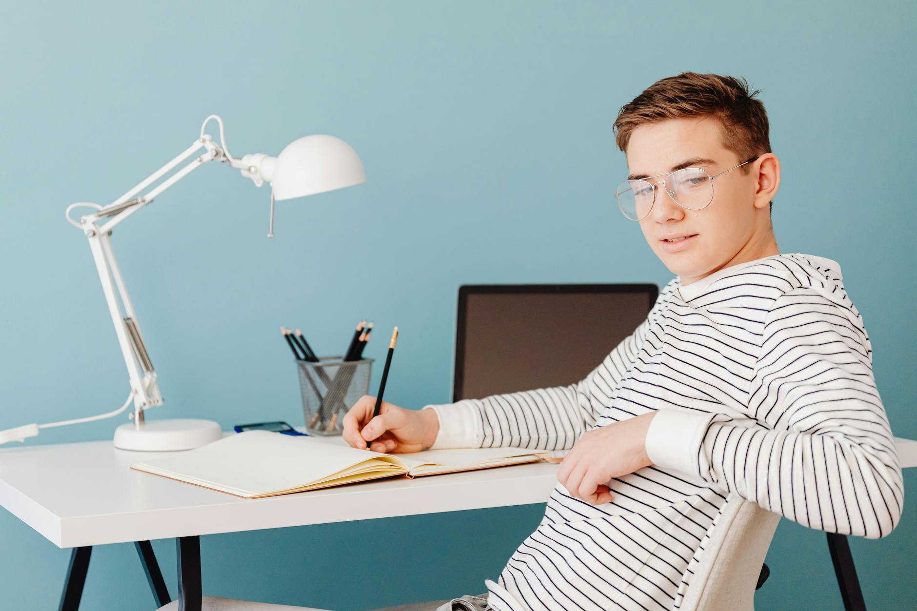 Young male student wearing glasses studying at a desk with a laptop and lamp — TransferCredit.org