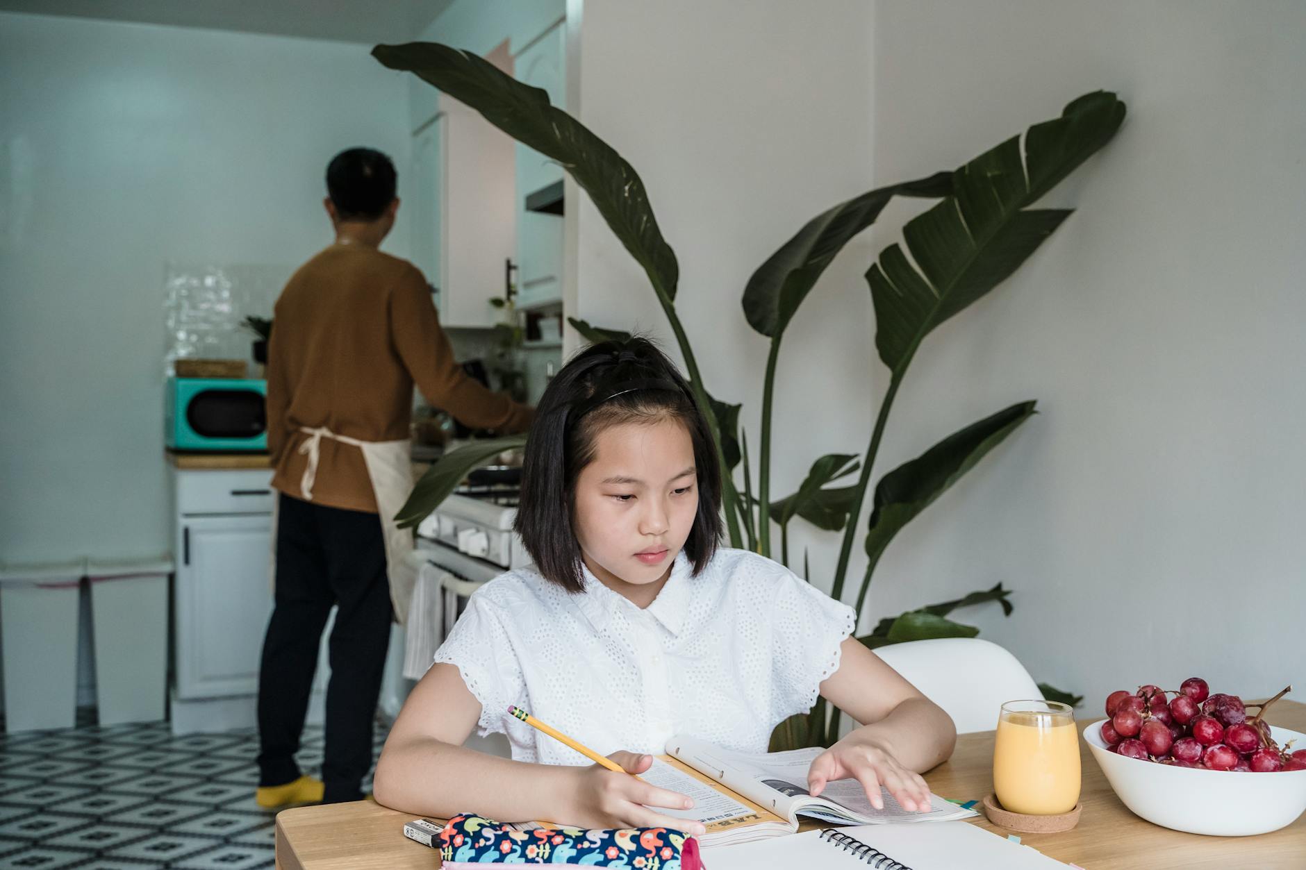 Girl focuses on homework at the kitchen table with fruit and juice nearby — TransferCredit.org