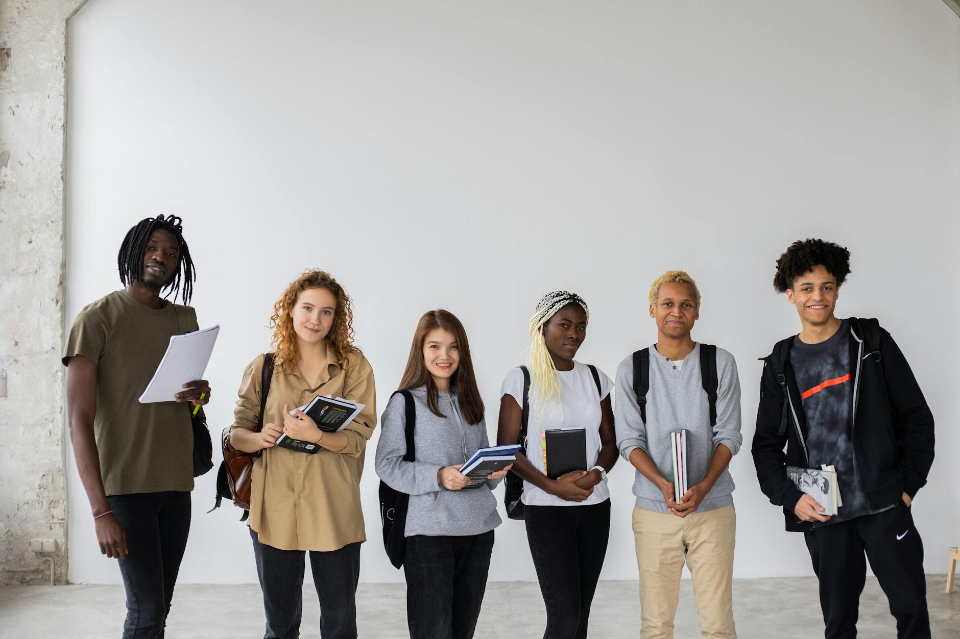 Group of diverse young multiracial classmates with notebooks and textbooks and backpacks smiling at camera — TransferCredit.org