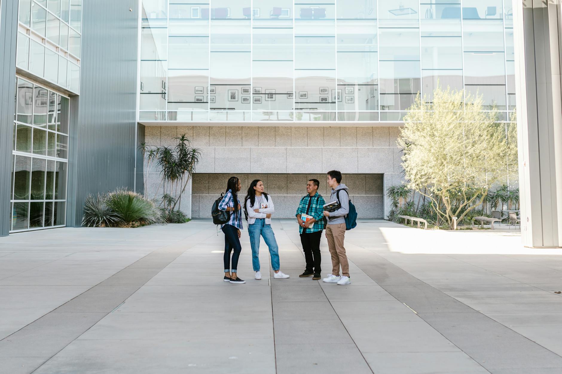 A group of diverse college students standing and talking in a sunny outdoor campus setting — TransferCredit.org