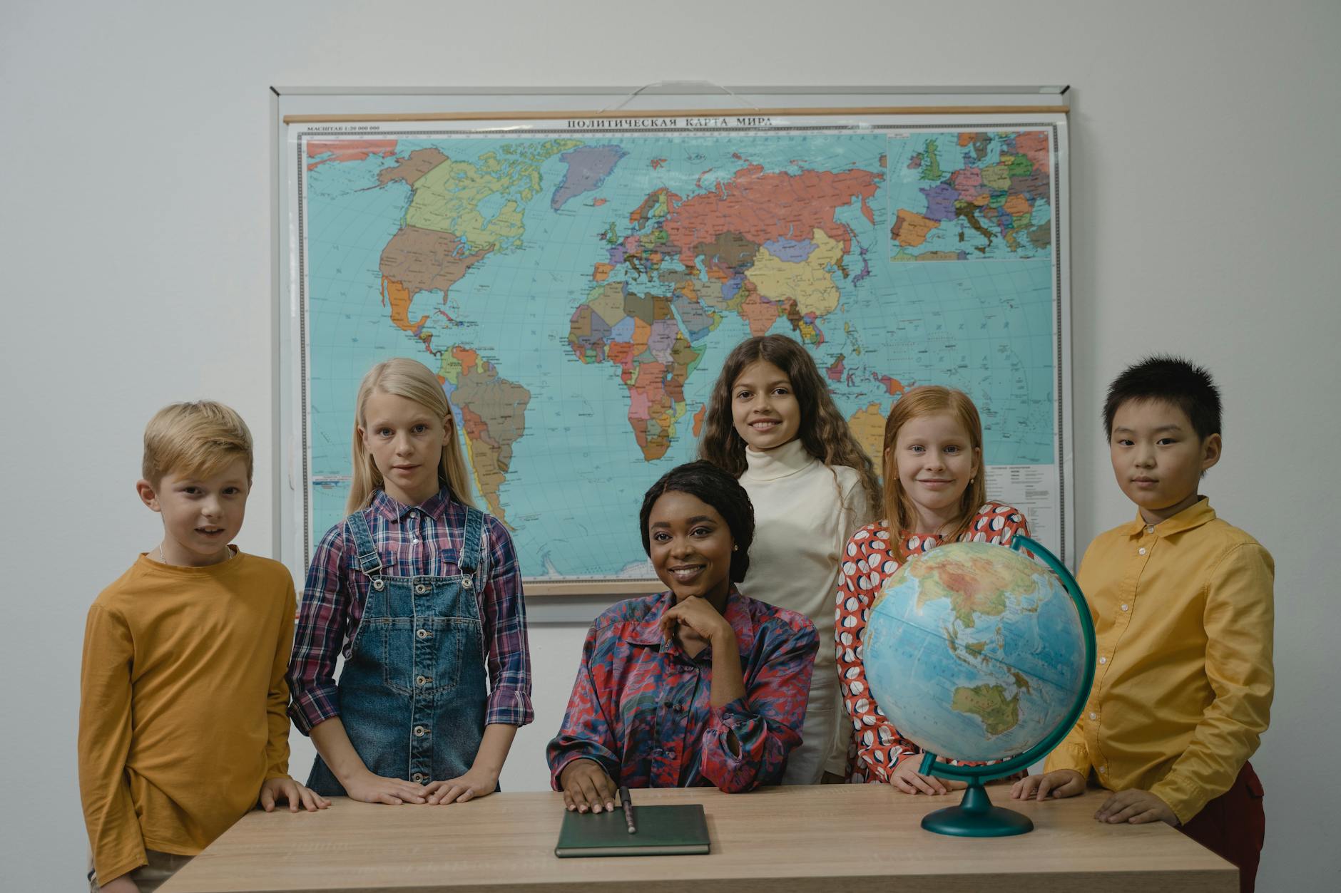 A diverse group of students with a teacher in a classroom setting featuring a globe and world map — TransferCredit.org