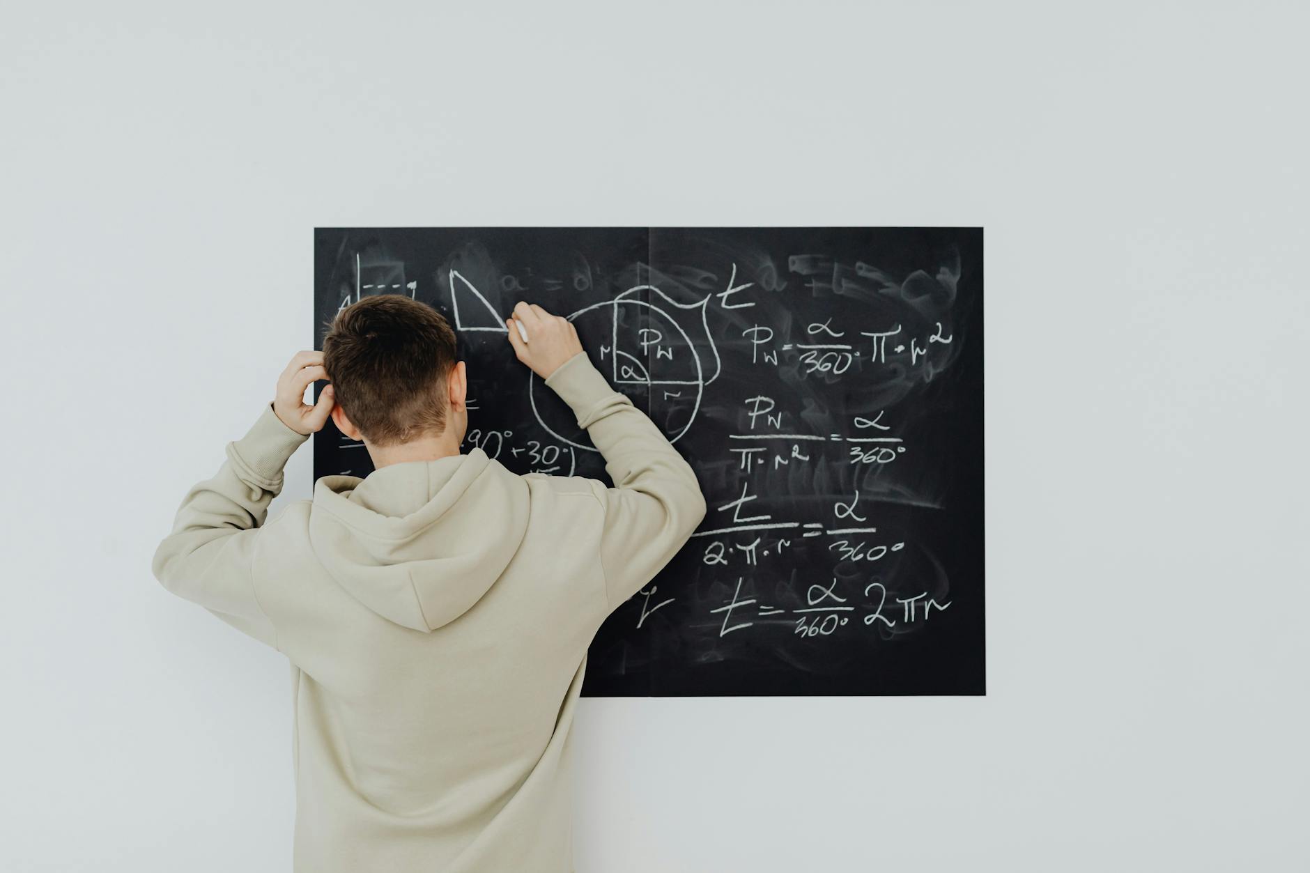 Teenager in hoodie writing math formulas on a blackboard indoors, showcasing problem-solving skills — TransferCredit.org