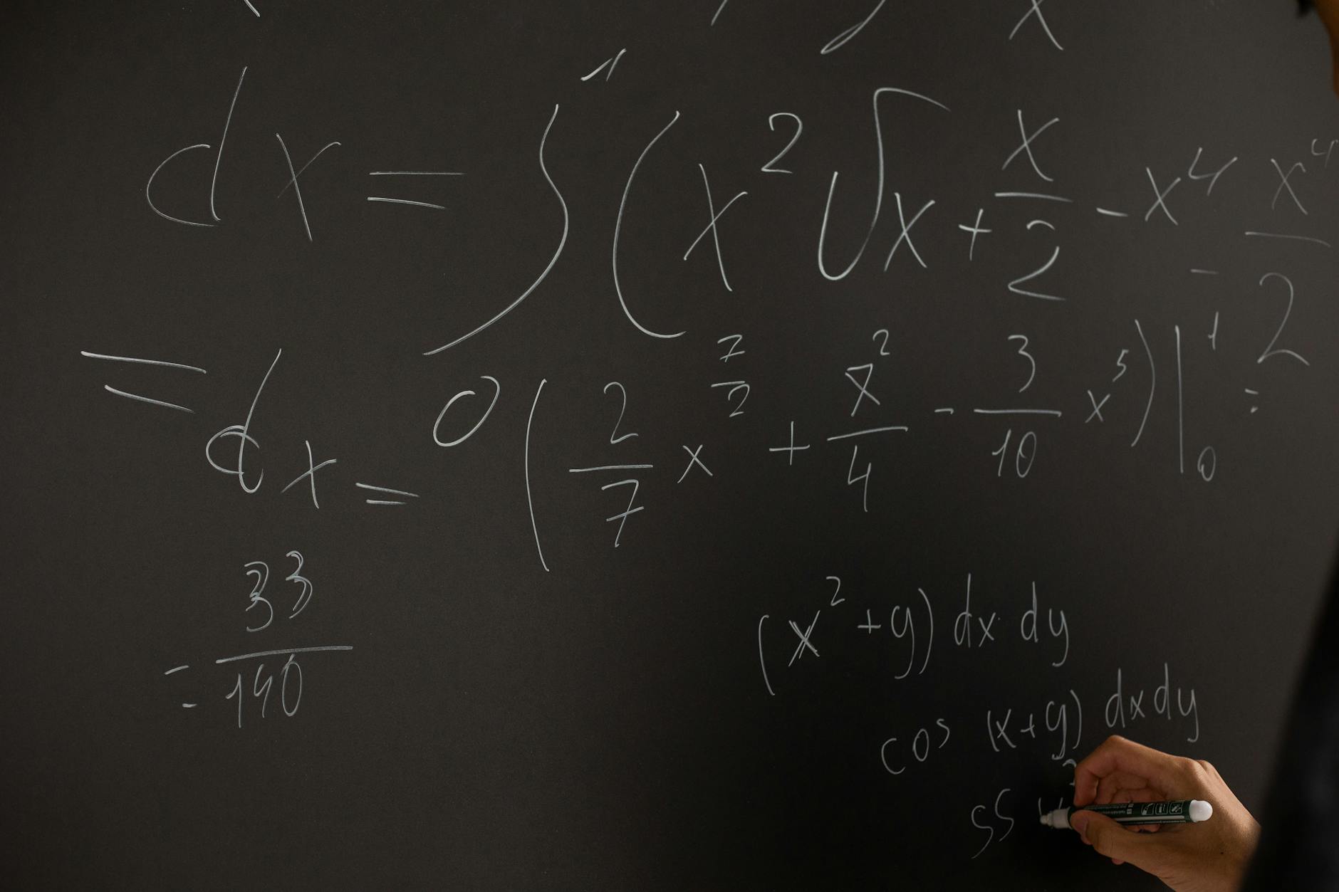 Close-up of hand writing complex math equations on a chalkboard in a classroom setting — TransferCredit.org