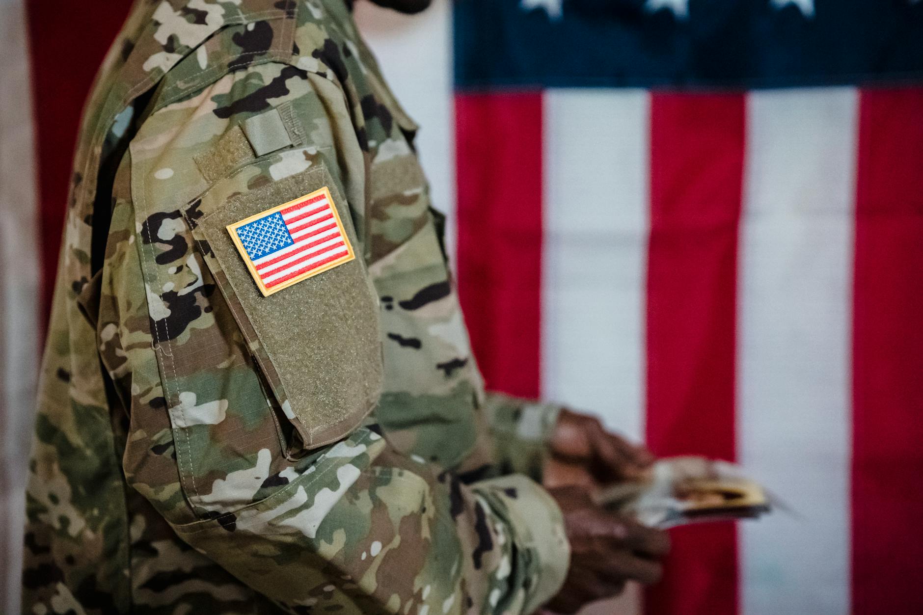 Close-up of a soldier in military uniform with American flag patch and background — TransferCredit.org