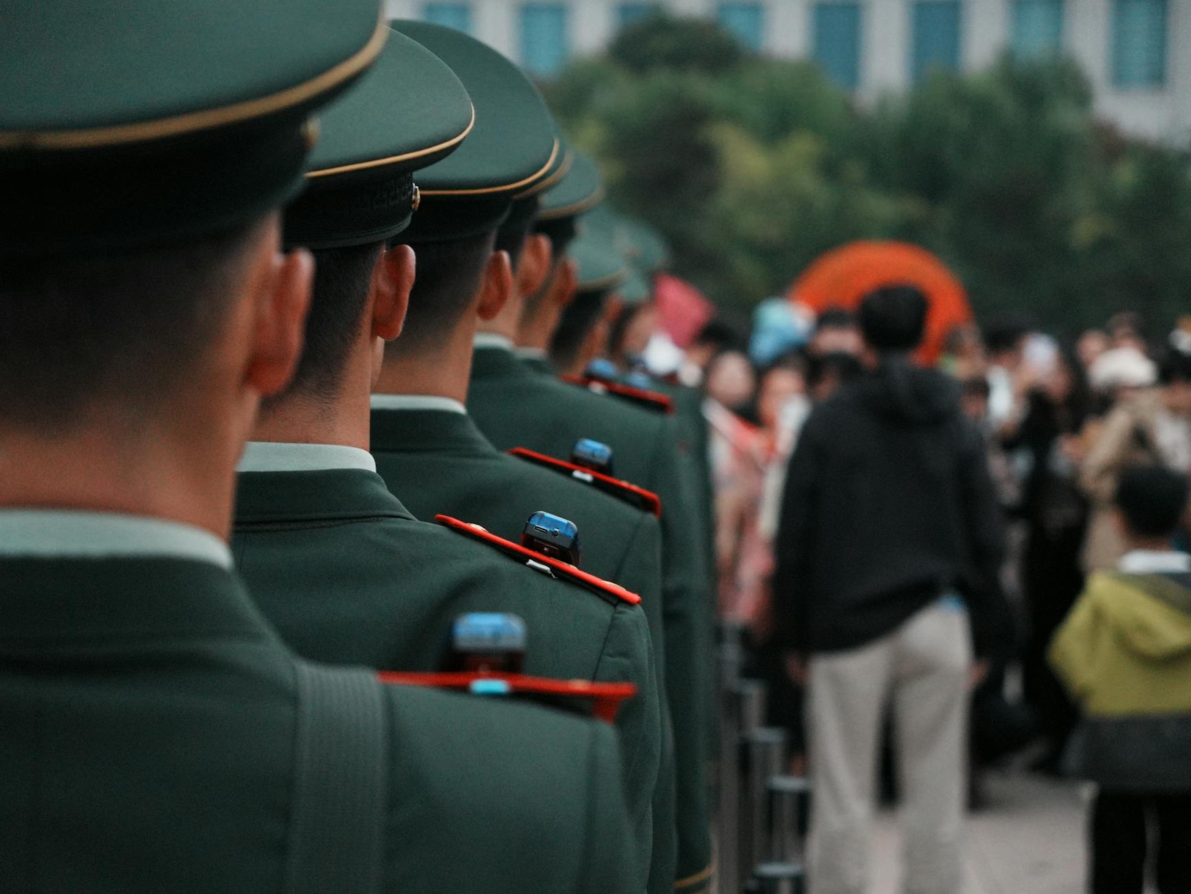 Military officers in green uniforms stand in line formation outdoors, facing a crowd — TransferCredit.org