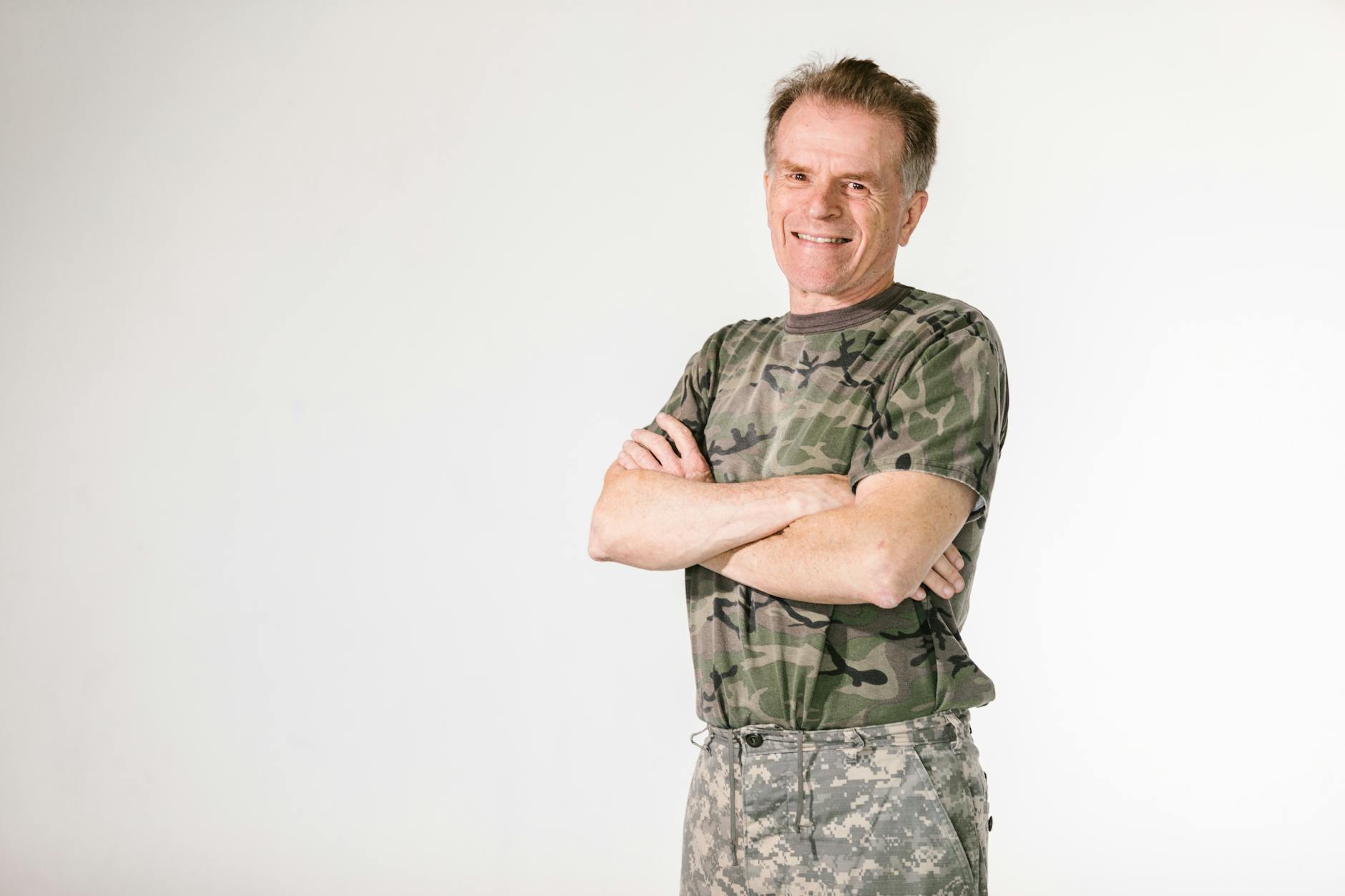 Smiling military veteran confidently posing in camouflage against a white background — TransferCredit.org