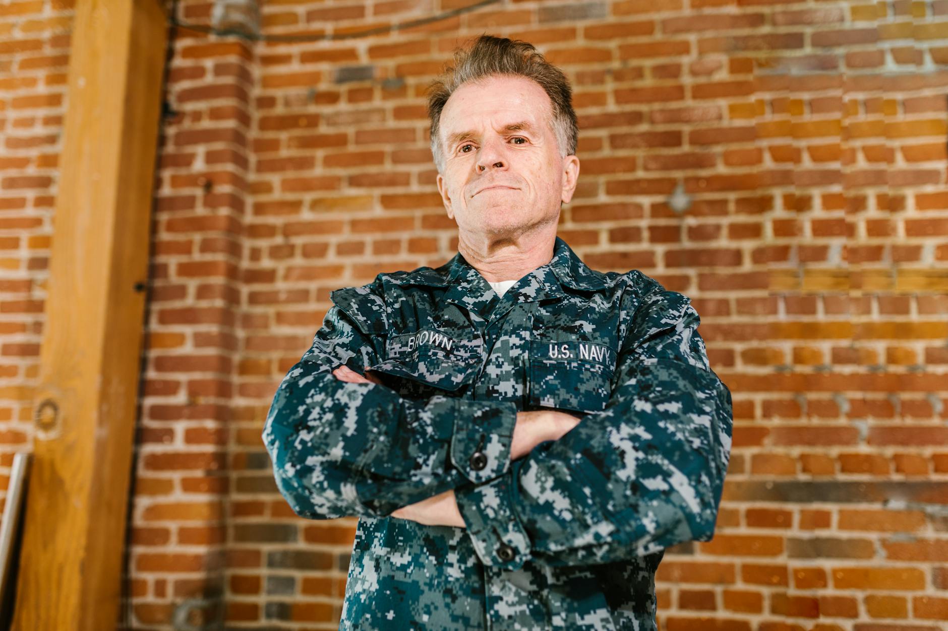 Proud US Navy veteran standing confidently in military uniform with brick background — TransferCredit.org