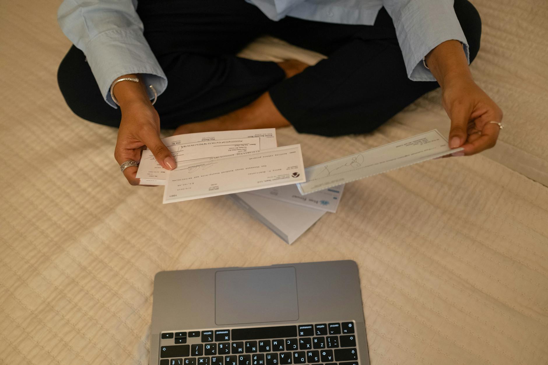 Close-up of hands holding cheques beside a laptop indoors for financial tasks — TransferCredit.org