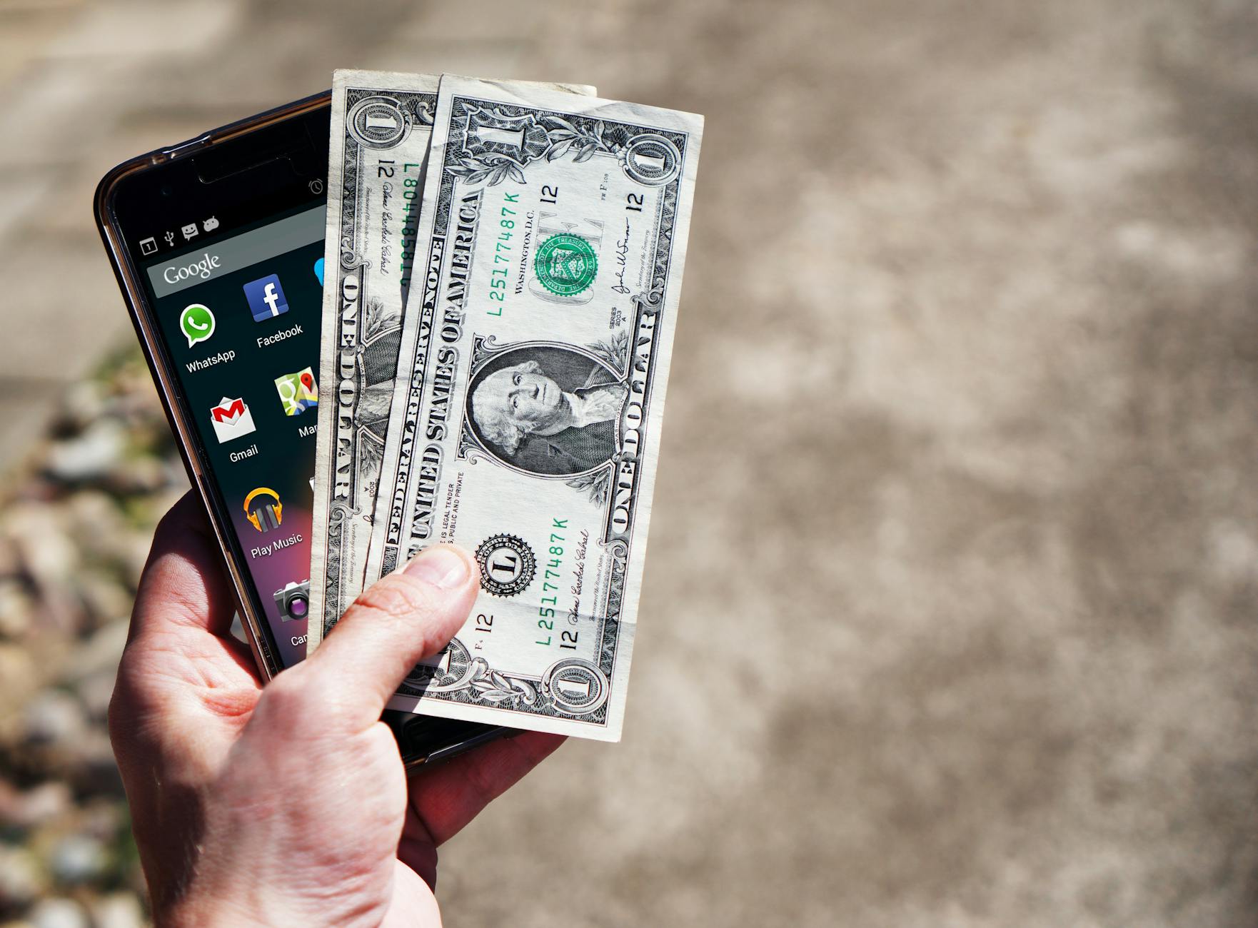 Close-up of a hand holding US dollar bills and a smartphone outdoors, showcasing financial technology — TransferCredit.org