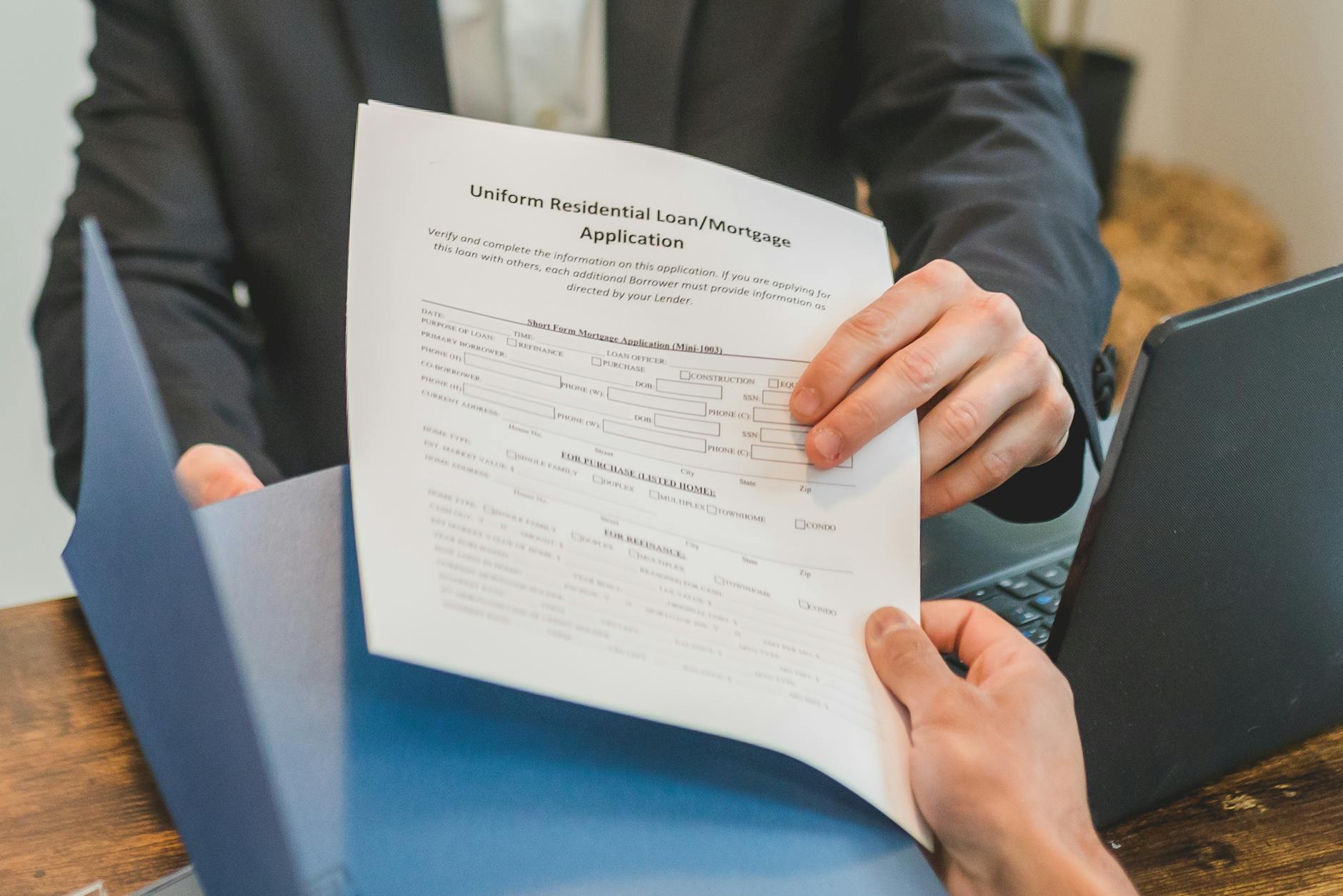 Professional setting showing hands exchanging a mortgage application document indoors — TransferCredit.org
