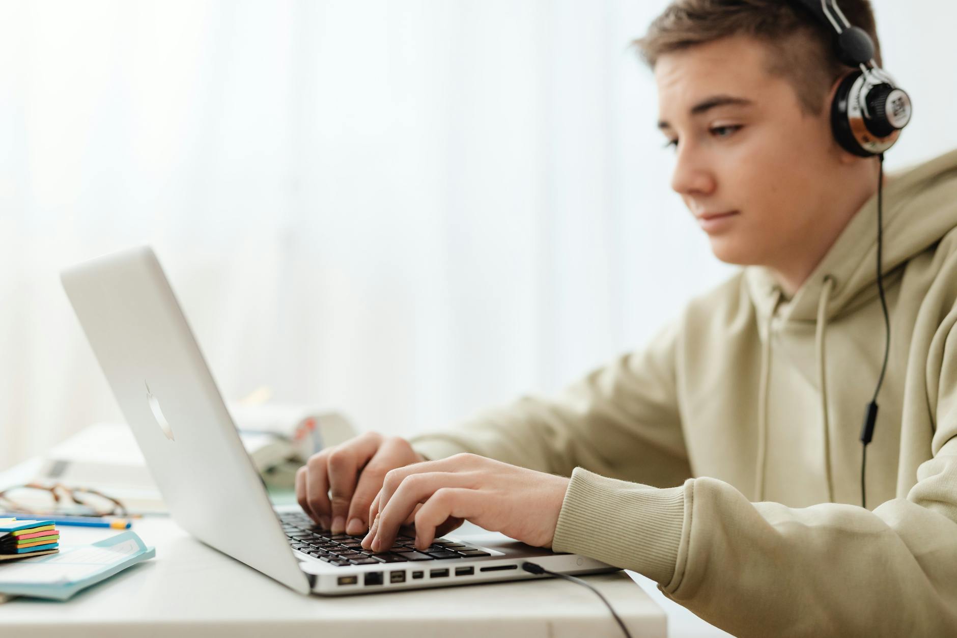 Teen using a laptop and headphones for online learning at home — TransferCredit.org