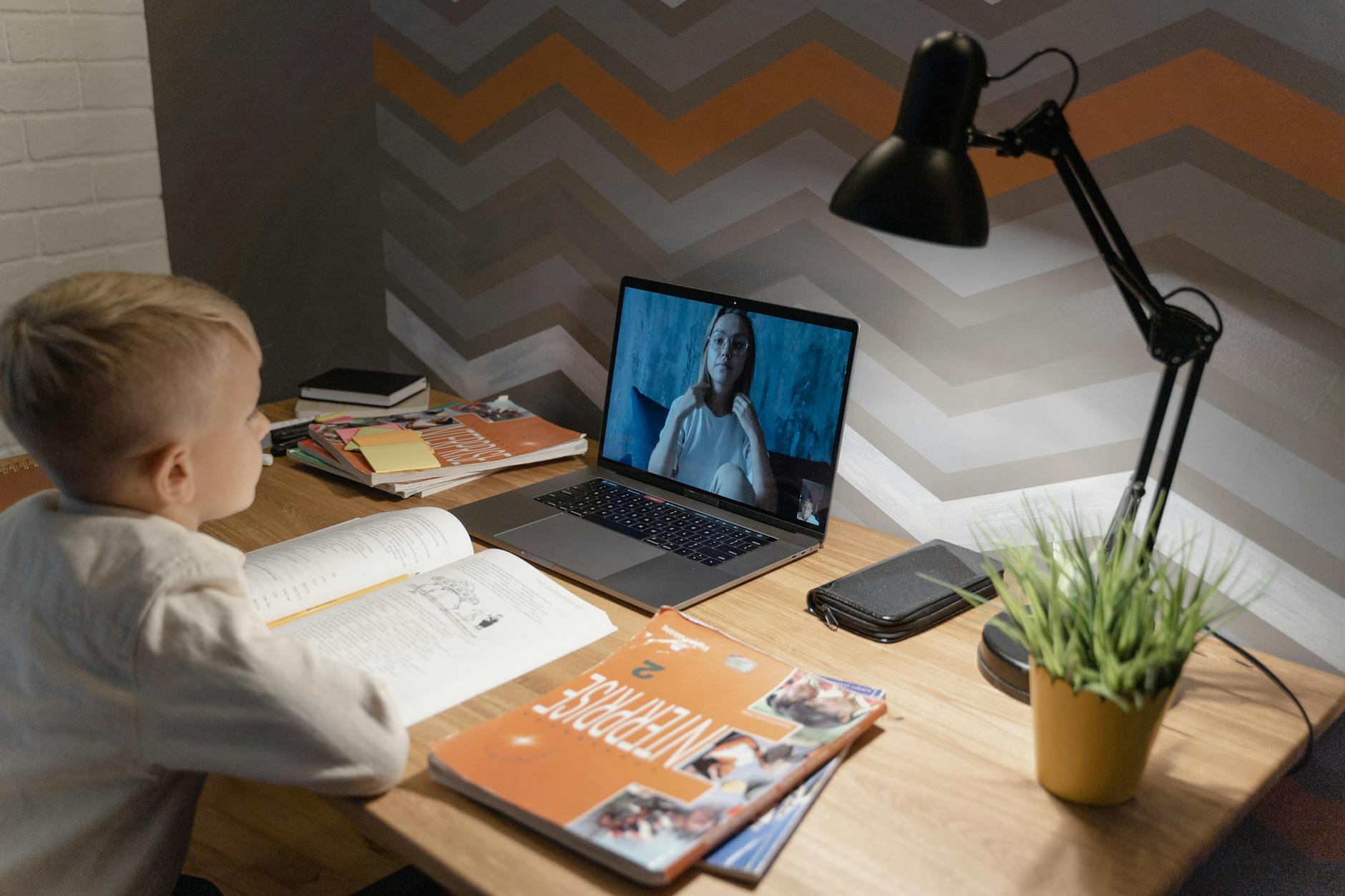 A young boy participates in a virtual class from home, using a laptop and study materials — TransferCredit.org