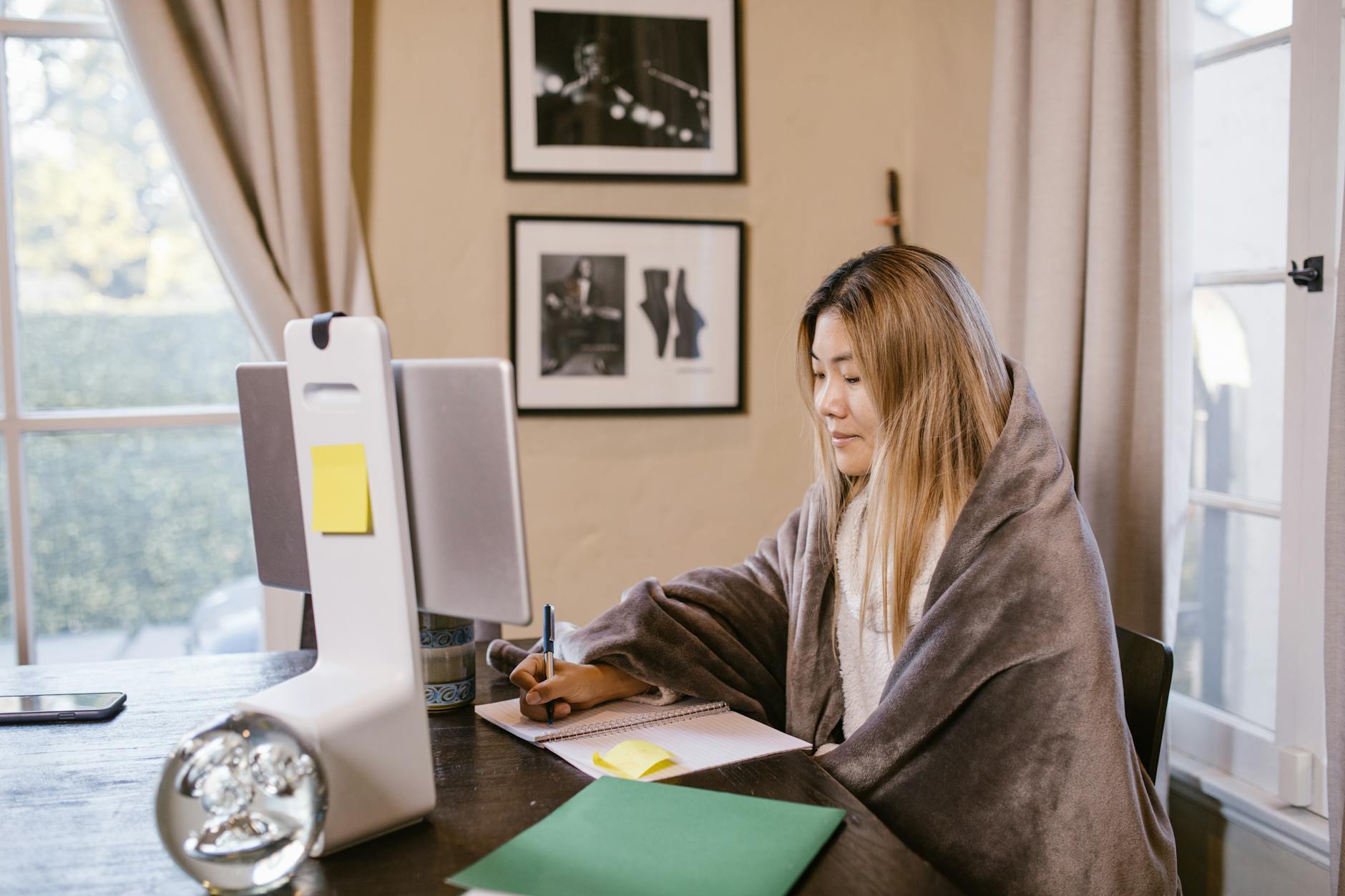 Asian woman focused on online learning at home, wrapped in a blanket with a notebook and computer — TransferCredit.org