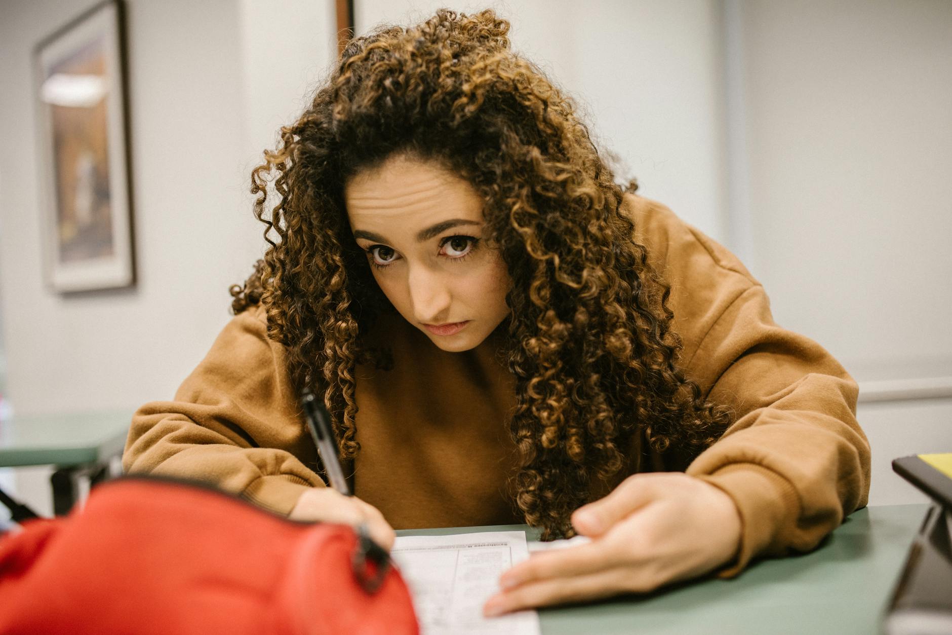 Female student deeply engaged in exam writing in a classroom setting — TransferCredit.org