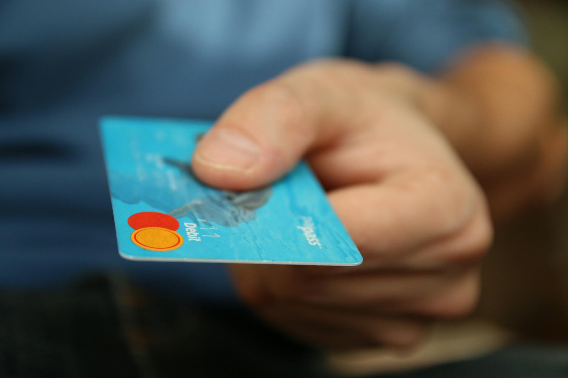 A close-up shot of a hand offering a blue debit card for payment — TransferCredit.org