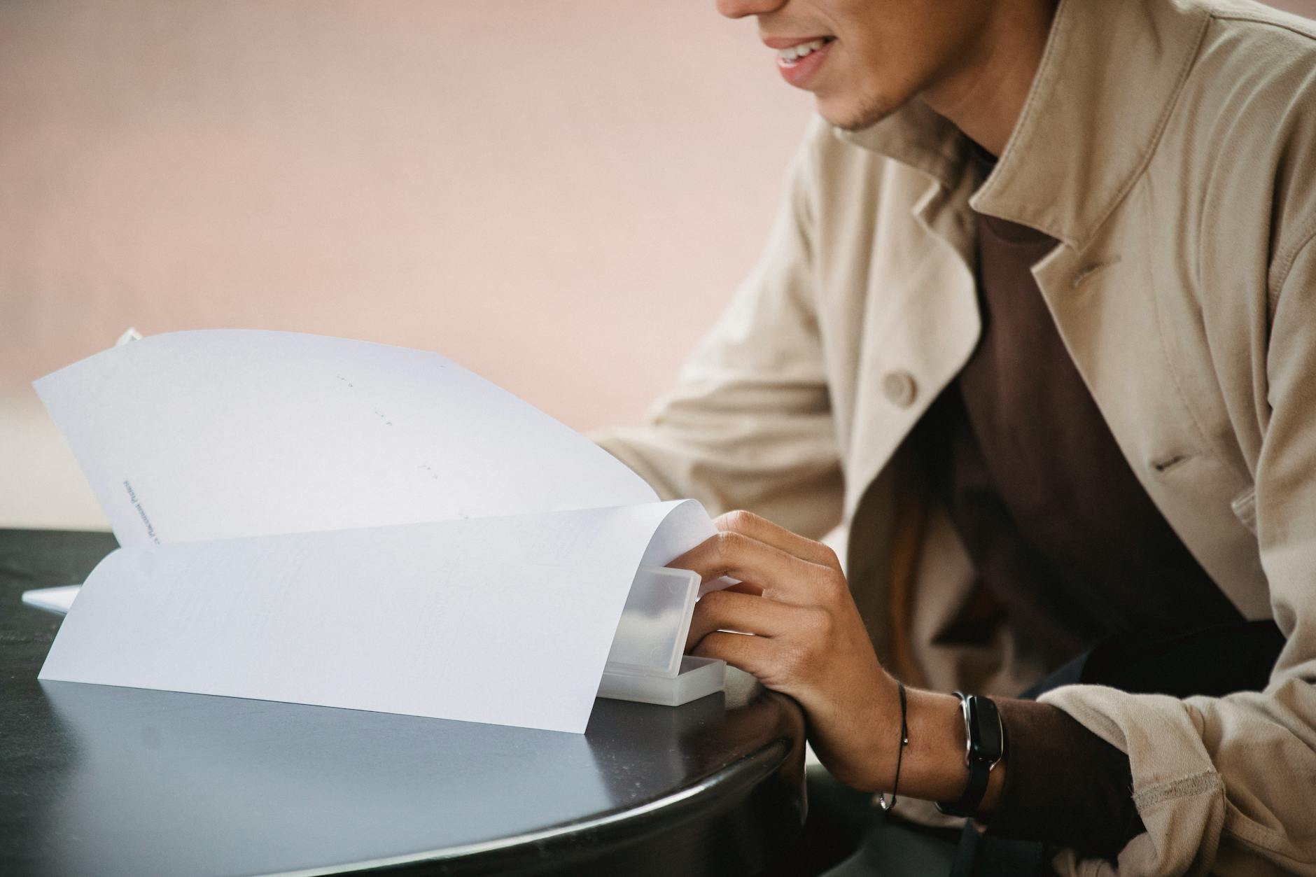 Side view of crop smiling male learner sitting at table and flipping pages of document with homework task — TransferCredit.org