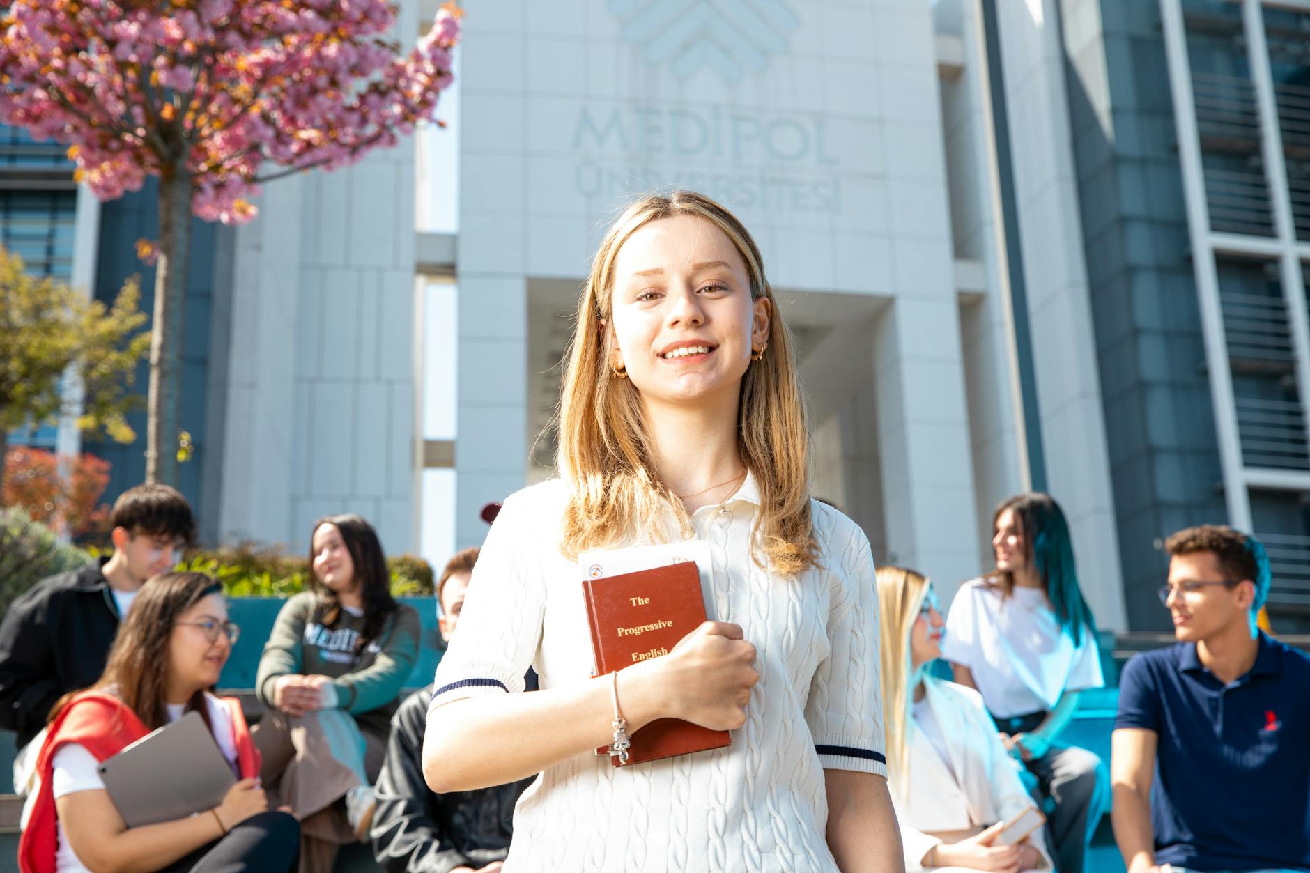 Happy university students socializing on campus, with a focus on a smiling young woman holding a book — TransferCredit.org