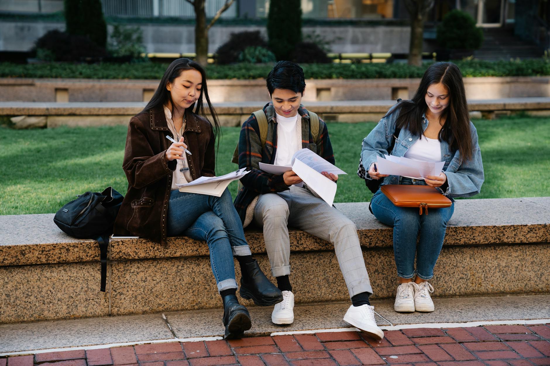 Three students studying together on a bench in a university campus setting outdoors — TransferCredit.org