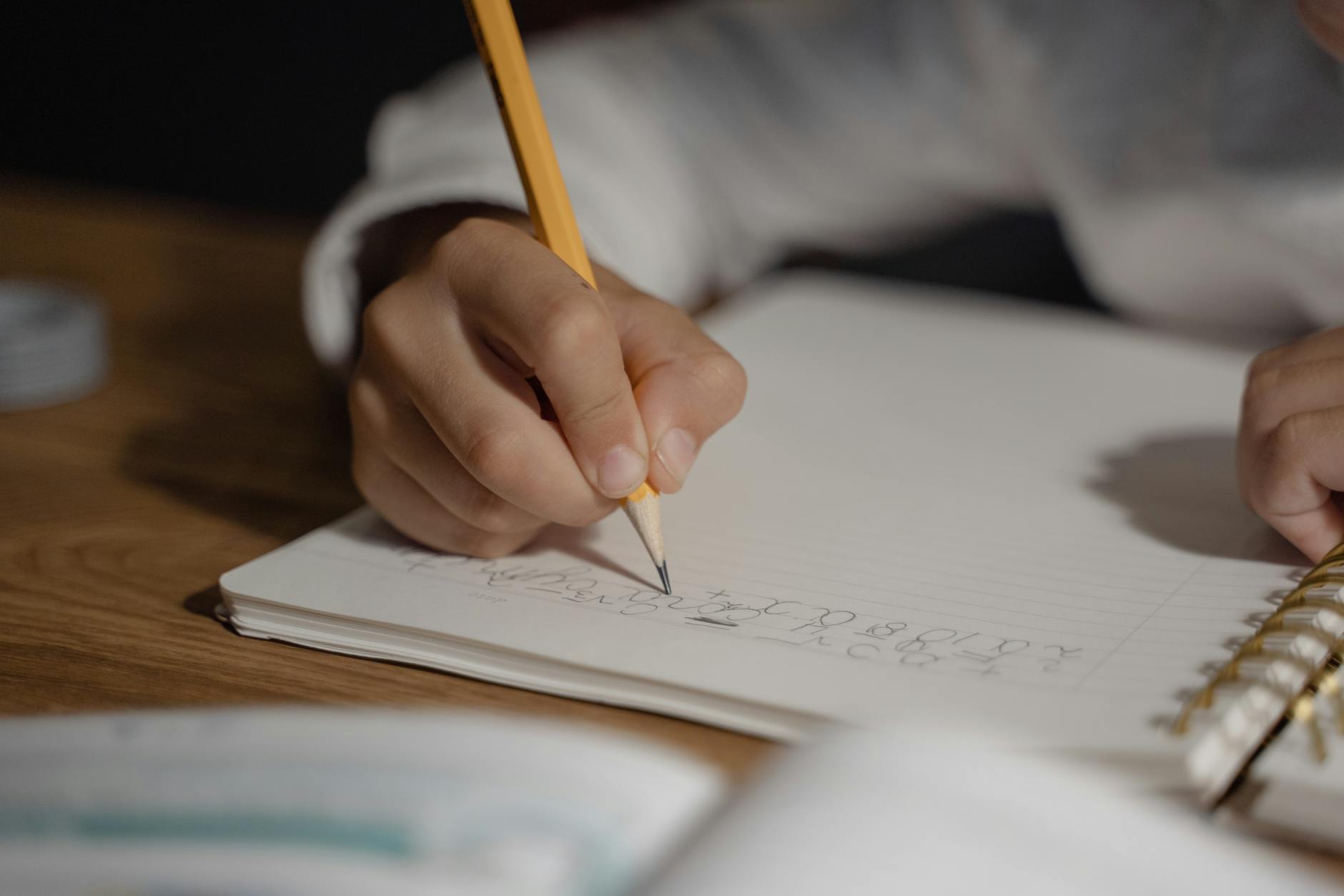 Close-up of a child writing homework using a pencil on a spiral notebook. Ideal for education themes — TransferCredit.org