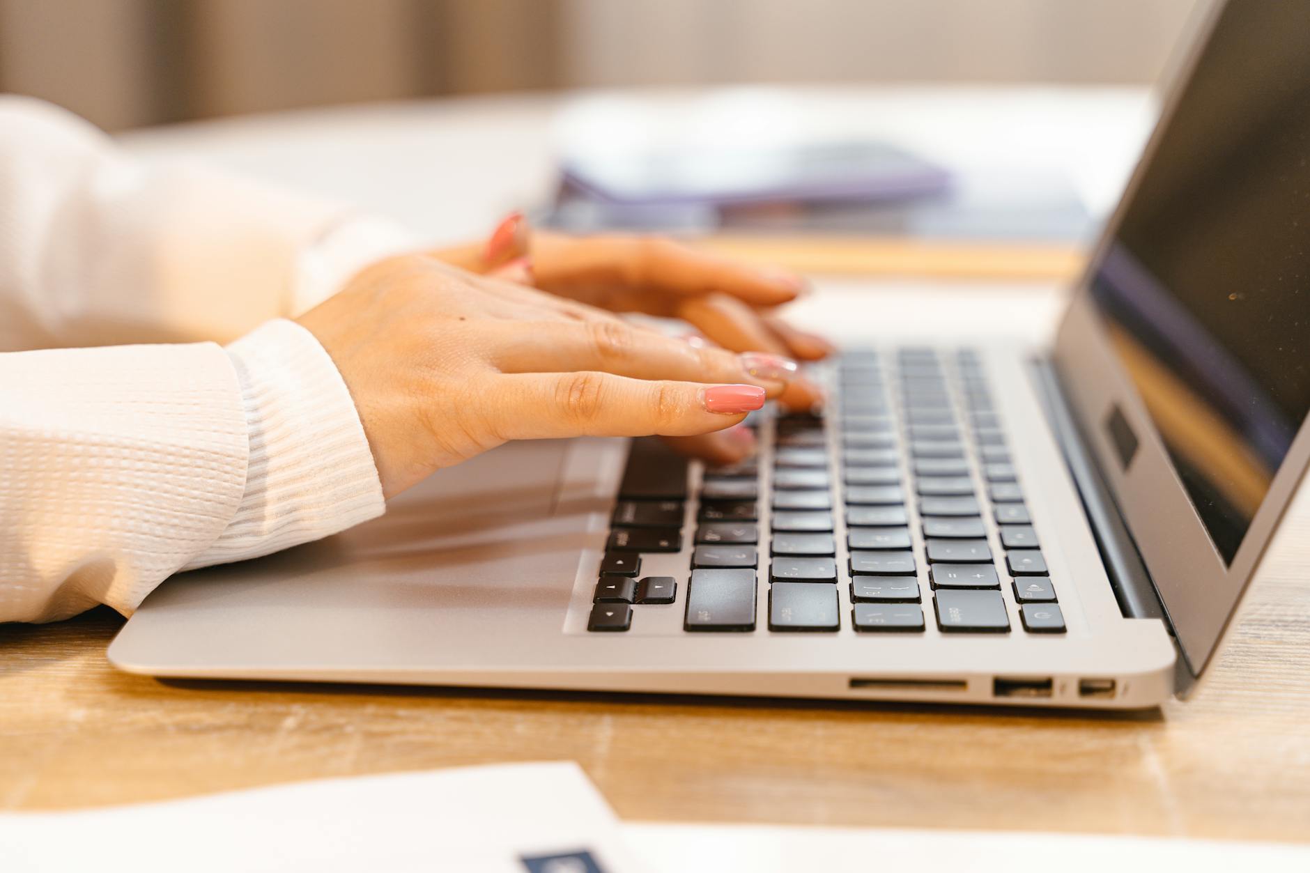 A close-up view of hands typing on a laptop keyboard with a focus on manicured nails and technology — TransferCredit.org